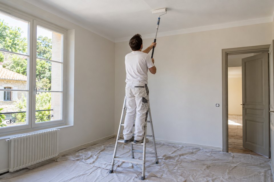 Peintre sur escabeau peignant un plafond au rouleau